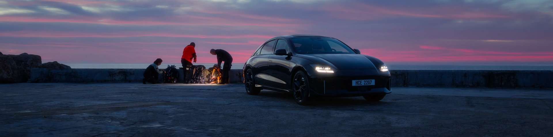 A Hyundai IONIQ 6 is parked at the beach with people in the background sorting through material.