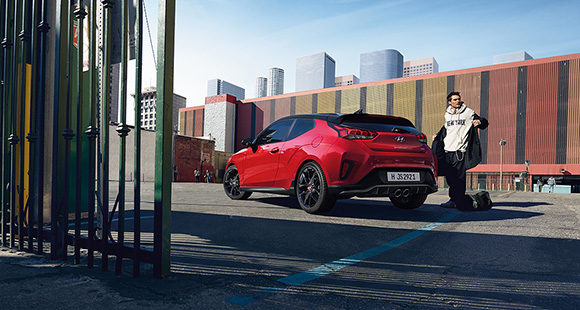 A man and left side rear view of red veloster parking on the road