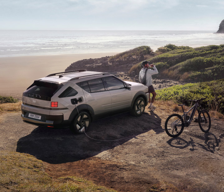 A man leaning against the bonnet of the all-new NEXO after a bicycle ride near the shore.