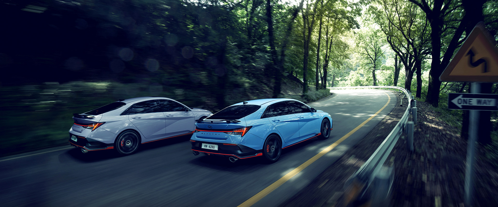 Two of New ELANTRA N, driving on a winding road, three-quarter rear view