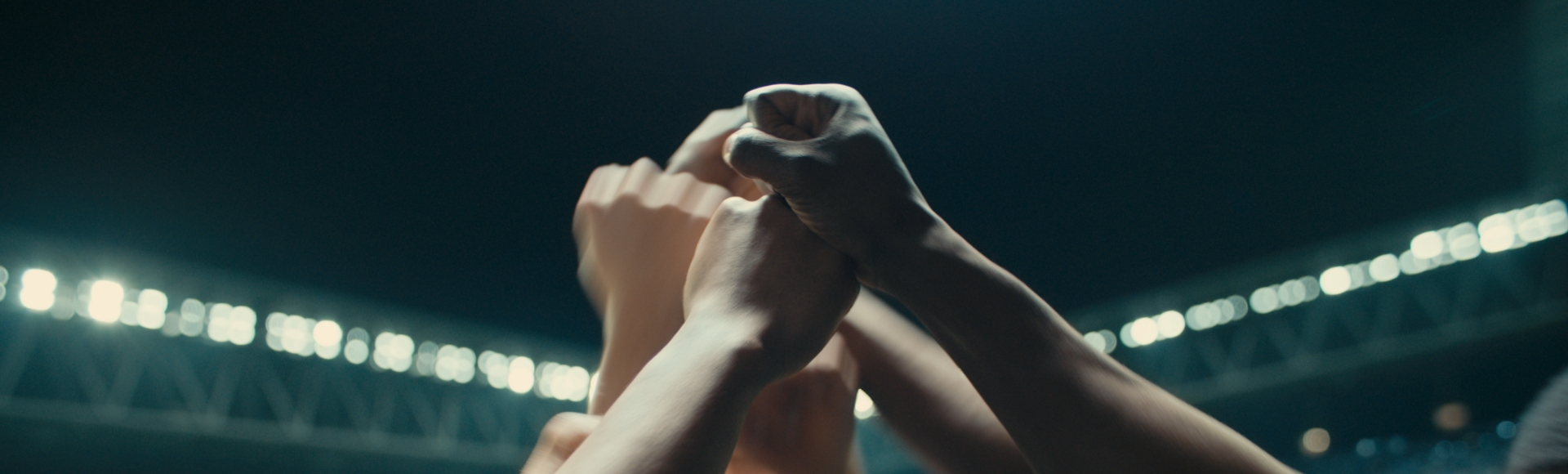 A collection of football players come together in the middle of a stadium to bump their fists in a show of solidarity.