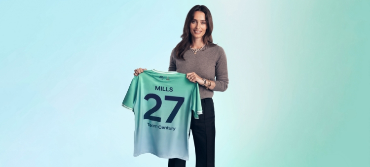 Ella Mills, the award-winning cookery author, entrepreneur, and champion of plant-based living, is holding her green and blue Team Century shirt where the number 27 is written on it.