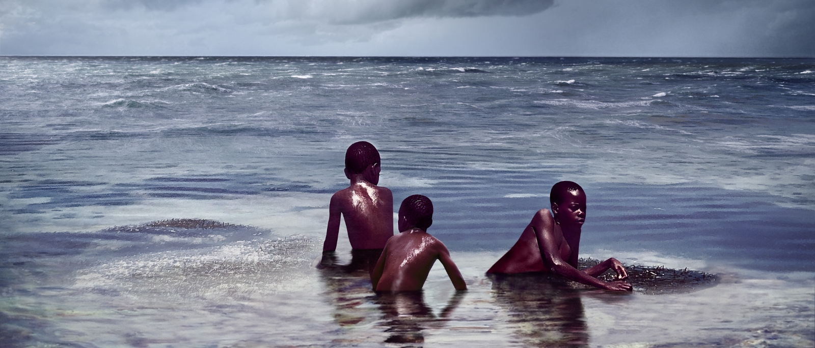 Three boys sitting on the last remaining piece of land surrounded by ocean. 